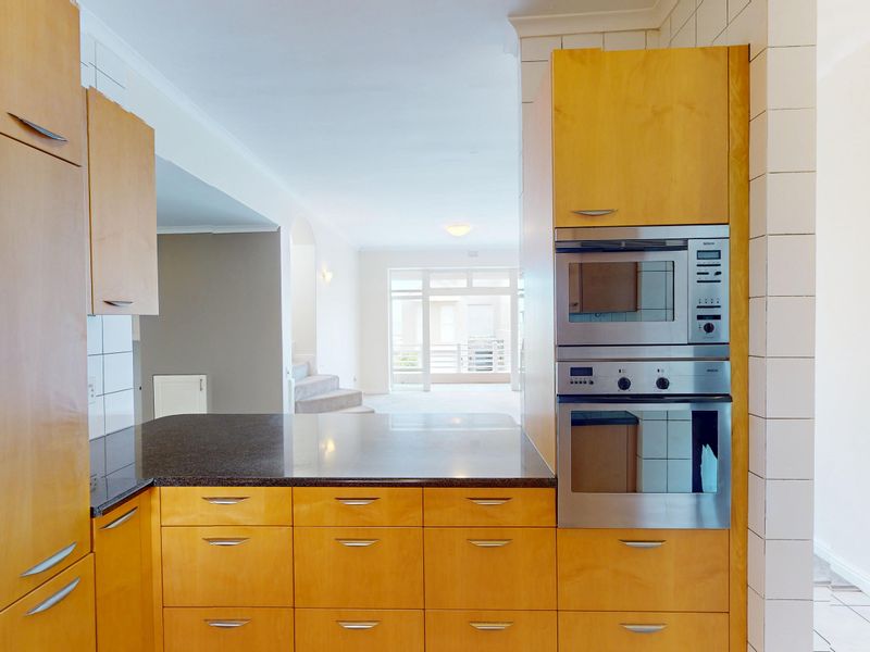 A functional kitchen featuring light wood cabinetry, granite countertops, and integrated stainless steel appliances, opening into a bright living area.