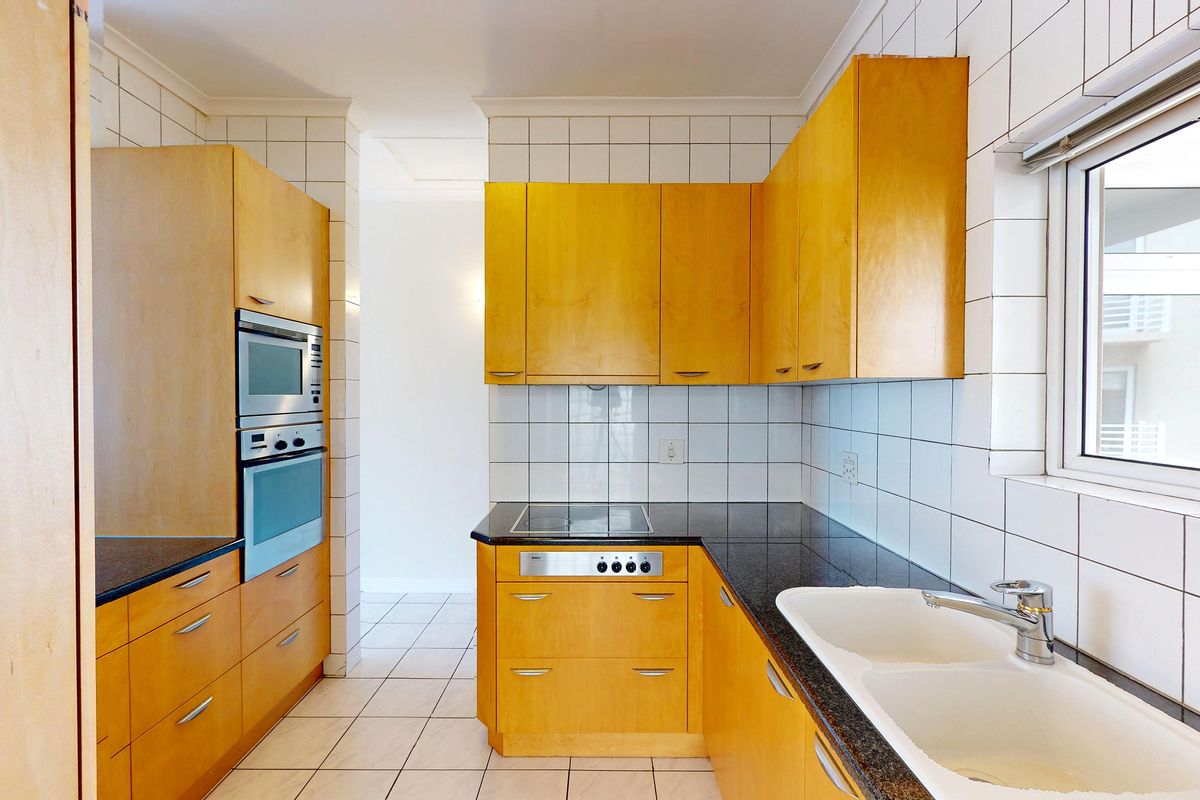 A functional kitchen featuring light wood cabinetry, granite countertops, a double basin sink, and built-in appliances including an oven and hob.