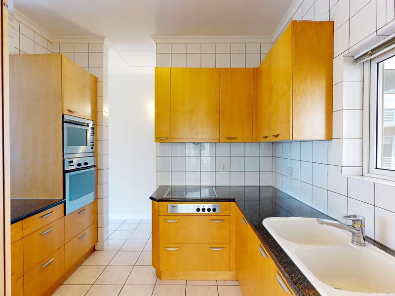 A functional kitchen featuring light wood cabinetry, granite countertops, a double basin sink, and built-in appliances including an oven and hob.