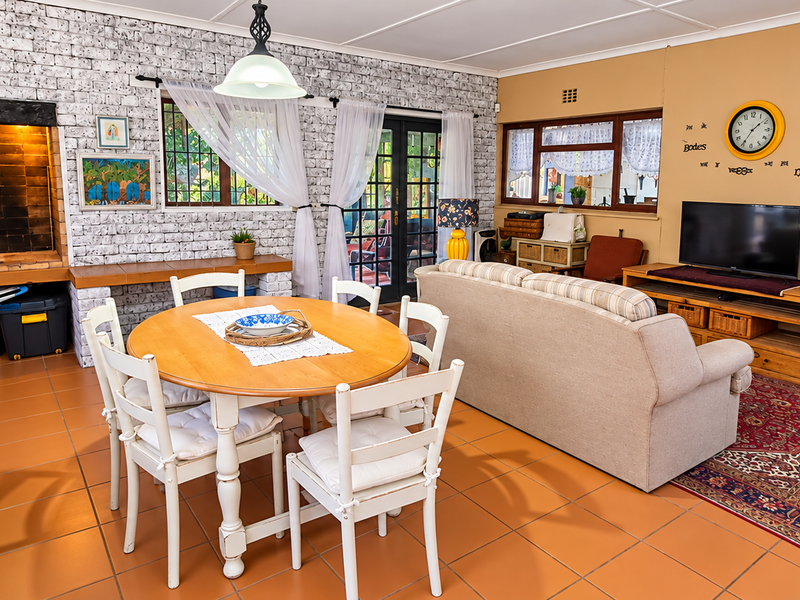 Spacious open-plan living and dining area featuring a built-in indoor braai, brick feature wall, and tiled flooring with direct access to the patio.