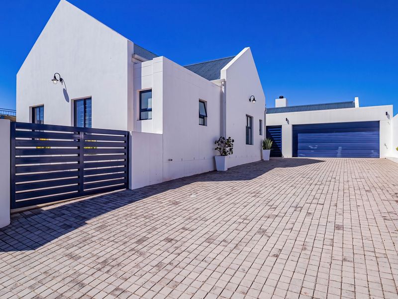 Modern front elevation featuring a paved driveway, secure metal gate, and integrated garage with clean white architectural lines.