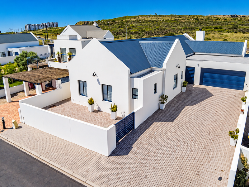 A well-maintained modern house featuring a clean white facade, corrugated metal roof, spacious paved driveway, and a private enclosed courtyard area.