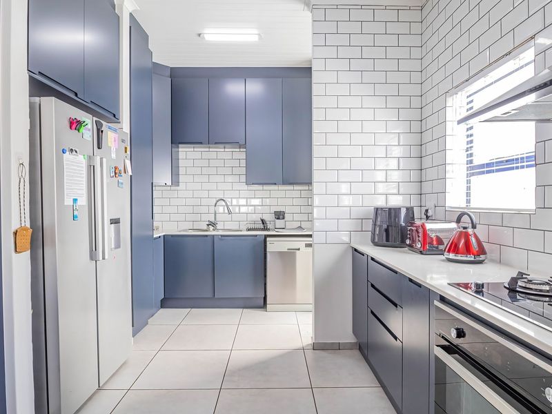 Modern kitchen featuring dark blue cabinetry, white subway tile backsplash, stone countertops, and integrated stainless steel appliances.