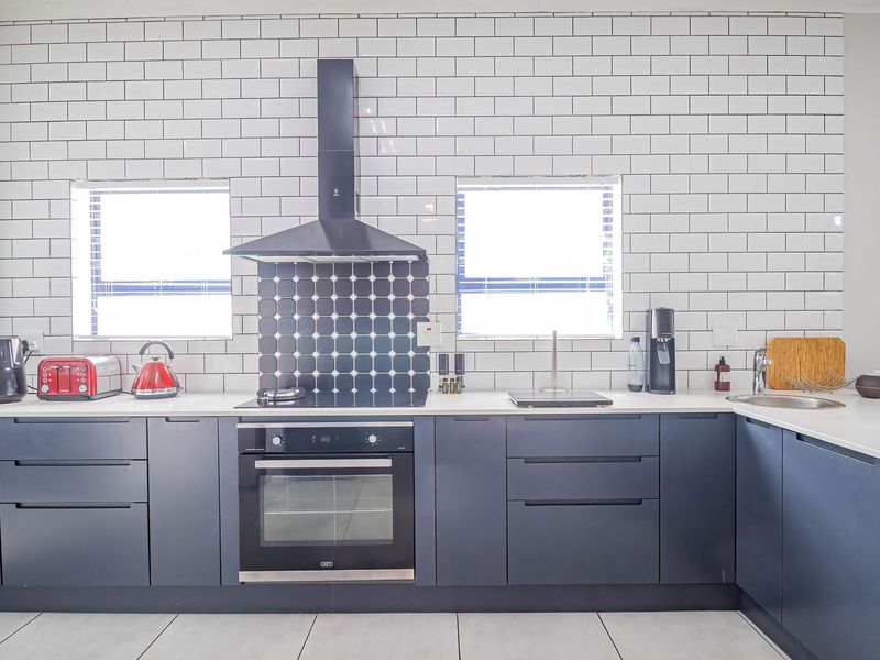 Modern kitchen featuring dark cabinetry, white quartz countertops, subway tile backsplash, built-in oven, and a sleek extractor fan.