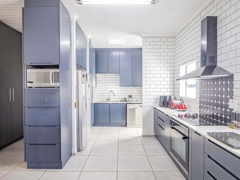 Modern kitchen featuring sleek blue cabinetry, white subway tile backsplash, integrated appliances, and clean tiled flooring with ample storage space.