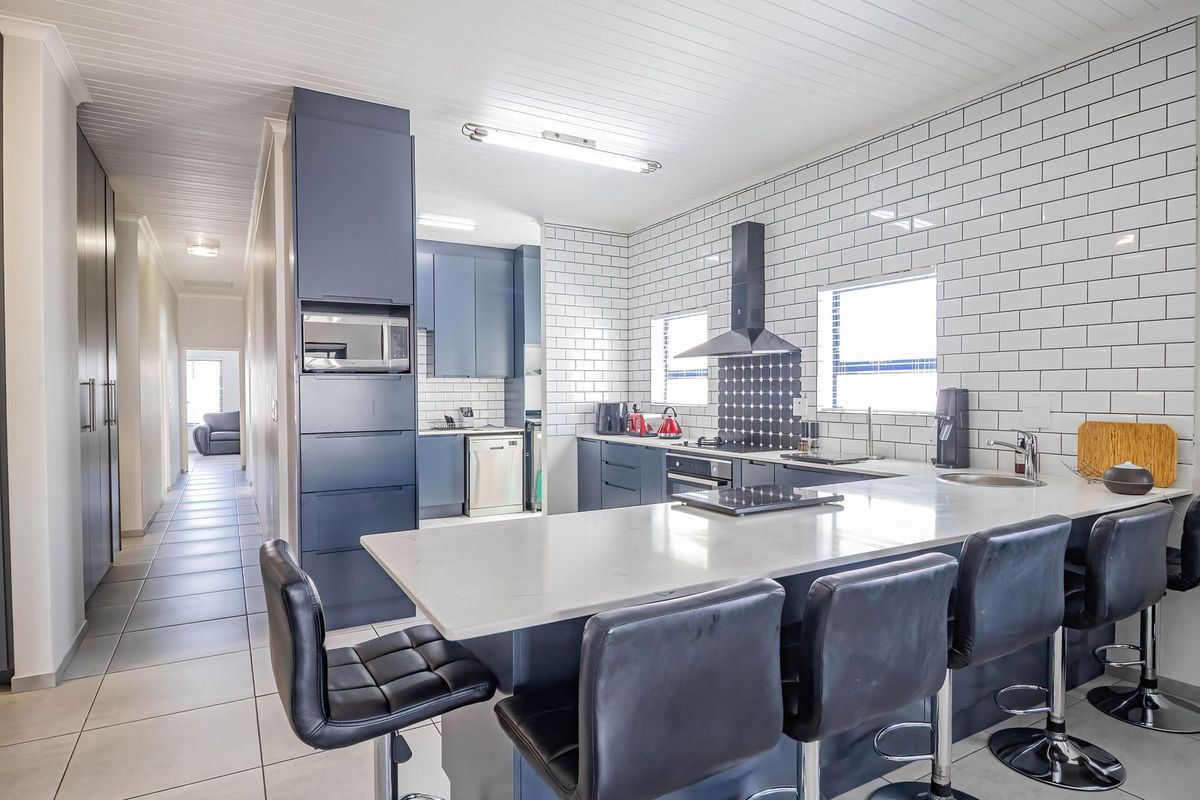 Modern kitchen featuring dark blue cabinetry, white subway tile backsplash, stone countertops, a central island, and integrated appliances with tiled flooring throughout.
