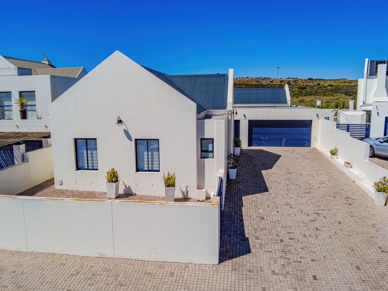 Aerial view of a modern house featuring a paved driveway, secure boundary walls, a double garage, and a clean white facade with a pitched roof.