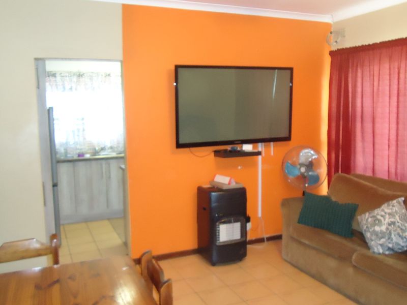 Open plan living area featuring tiled flooring and direct access to the kitchen, with a bright orange feature wall.