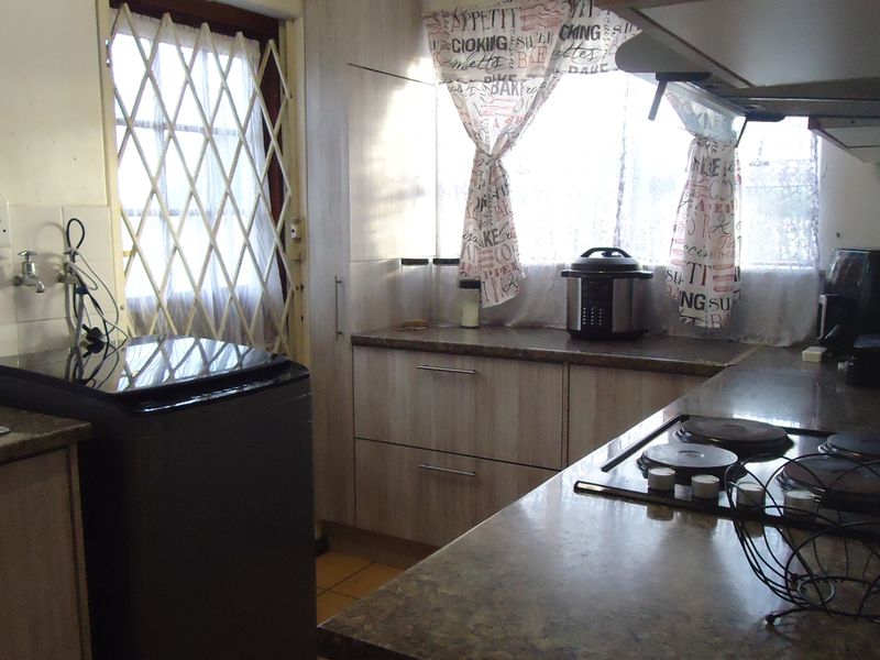 A functional kitchen featuring built-in cabinetry, laminate countertops, an electric hob with extractor fan, and a stainless steel sink with access to a security gate.