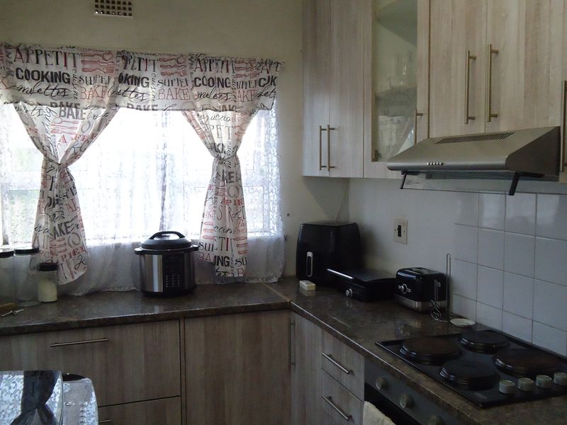 A functional kitchen featuring laminate cabinetry, granite countertops, a built-in electric hob, oven, and stainless steel extractor fan with a tiled backsplash.