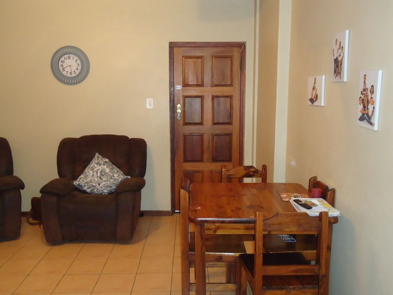 A living area featuring tiled flooring and a solid wooden door, providing a functional and neutral space for relaxation and dining.