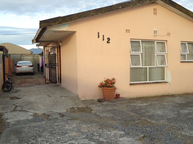 Front exterior view of a single-story house featuring a concrete driveway, security gate, and aluminium window frames, showing signs of exterior wear.