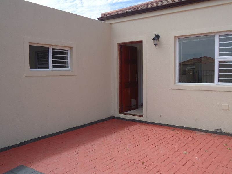 A rear exterior view featuring a paved patio area, exterior wall lighting, and access to the home through a wooden door.