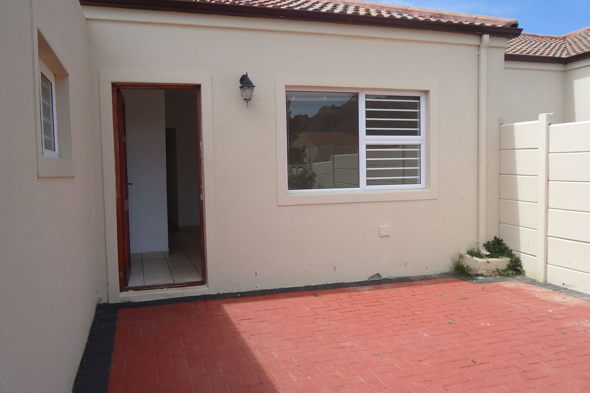 Rear exterior view featuring a paved patio area, security-fitted windows, and a tiled roof, providing a functional outdoor space.