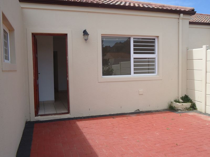 Rear exterior view featuring a paved patio area, security-fitted windows, and a tiled roof, providing a functional outdoor space.