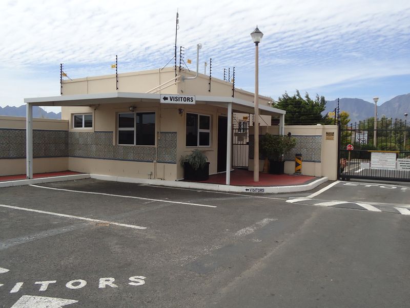 A secure estate entrance featuring a visitor parking area, gated access control, electric fencing, and a covered guardhouse structure.