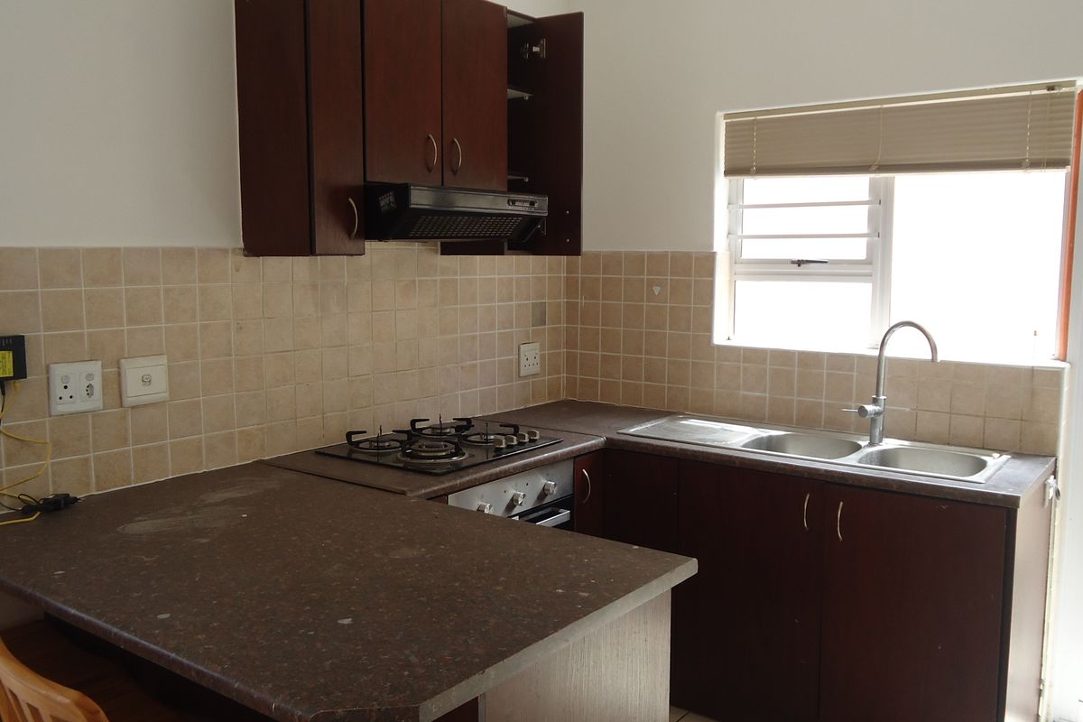 A functional kitchen featuring dark wood cabinetry, laminate countertops, a gas hob, and a double bowl sink with tiled backsplash and natural light.