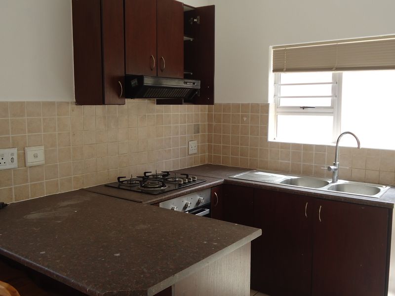A functional kitchen featuring dark wood cabinetry, laminate countertops, a gas hob, and a double bowl sink with tiled backsplash and natural light.