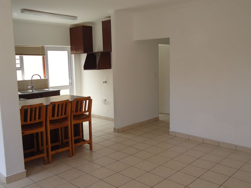 An open-plan living and kitchen area featuring tiled flooring, built-in cabinetry, and a breakfast counter, offering a functional and versatile space.