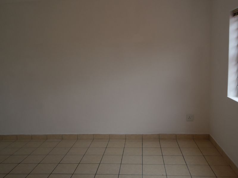 An empty bedroom featuring neutral tiled flooring, plain walls, and a window fitted with security bars.