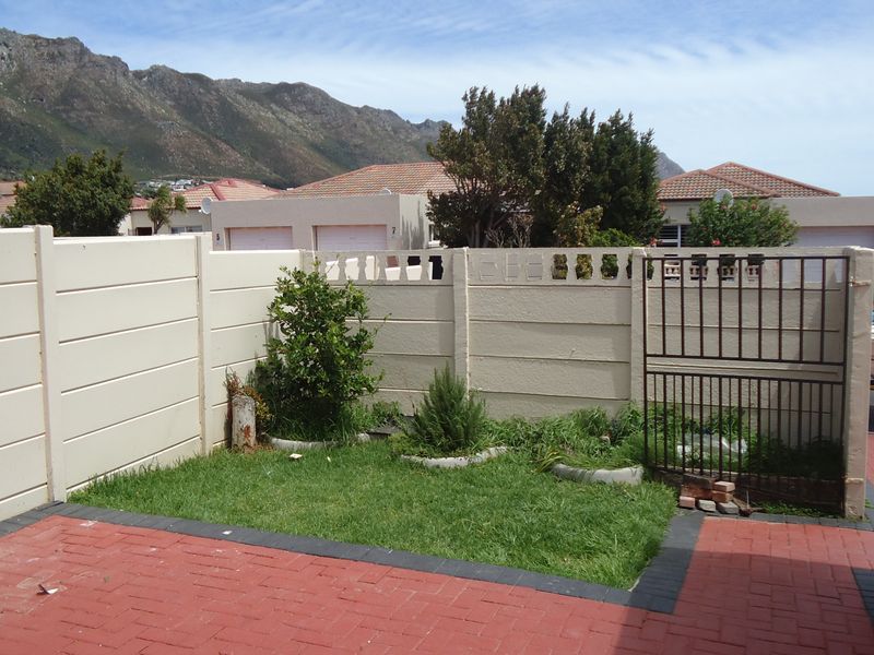 A private rear courtyard featuring a paved patio area, a small lawn, and secure precast concrete boundary walling with a metal access gate.