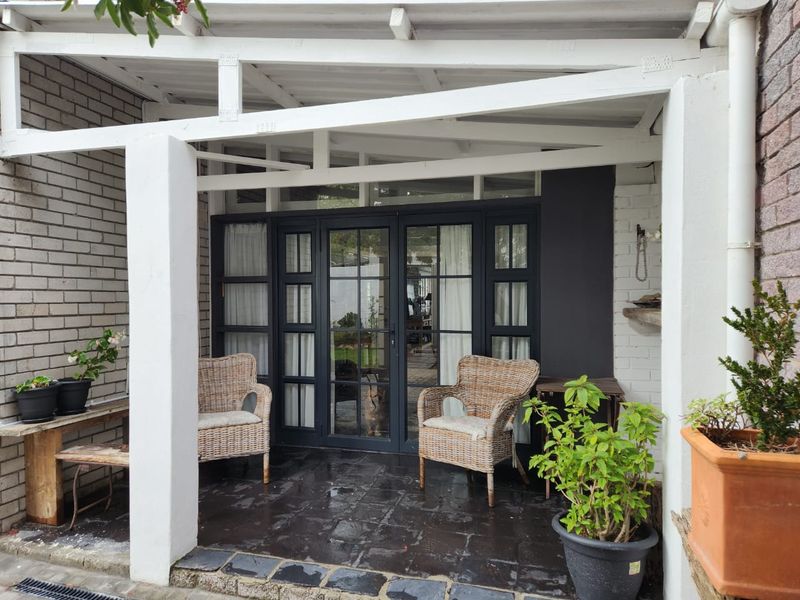 A covered patio area featuring dark tiled flooring, a white timber pergola structure, and dark-framed glass double doors leading into the home.