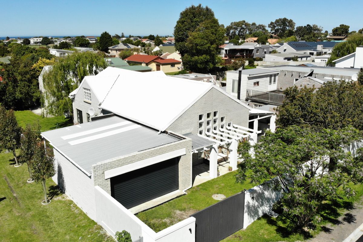 Aerial view of a modern residential property featuring a white metal roof, brick facade, attached garage, and a pergola-covered entrance area.