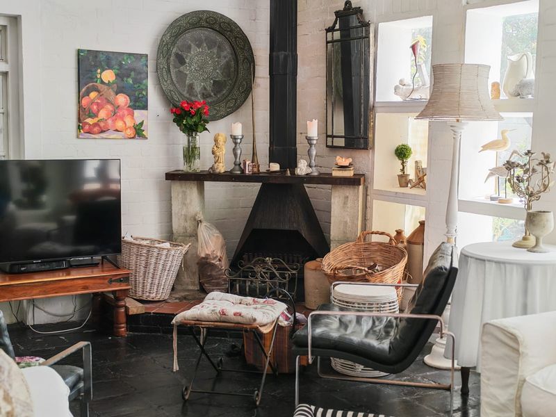 A cozy living room featuring a prominent black metal fireplace, exposed white brick walls, and dark tiled flooring with large windows.