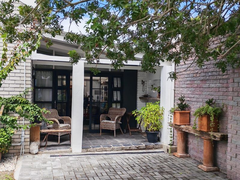 A covered patio area featuring brick paving, white structural pillars, and direct access to the interior through glass-paned doors.