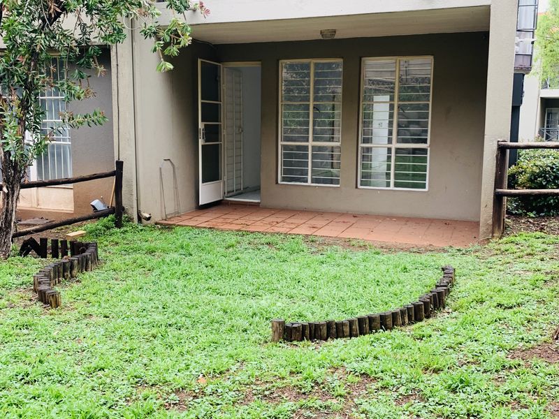 Rear view of the apartment featuring a ground-floor tiled patio, a first-floor balcony with metal railings, and a small private garden area.