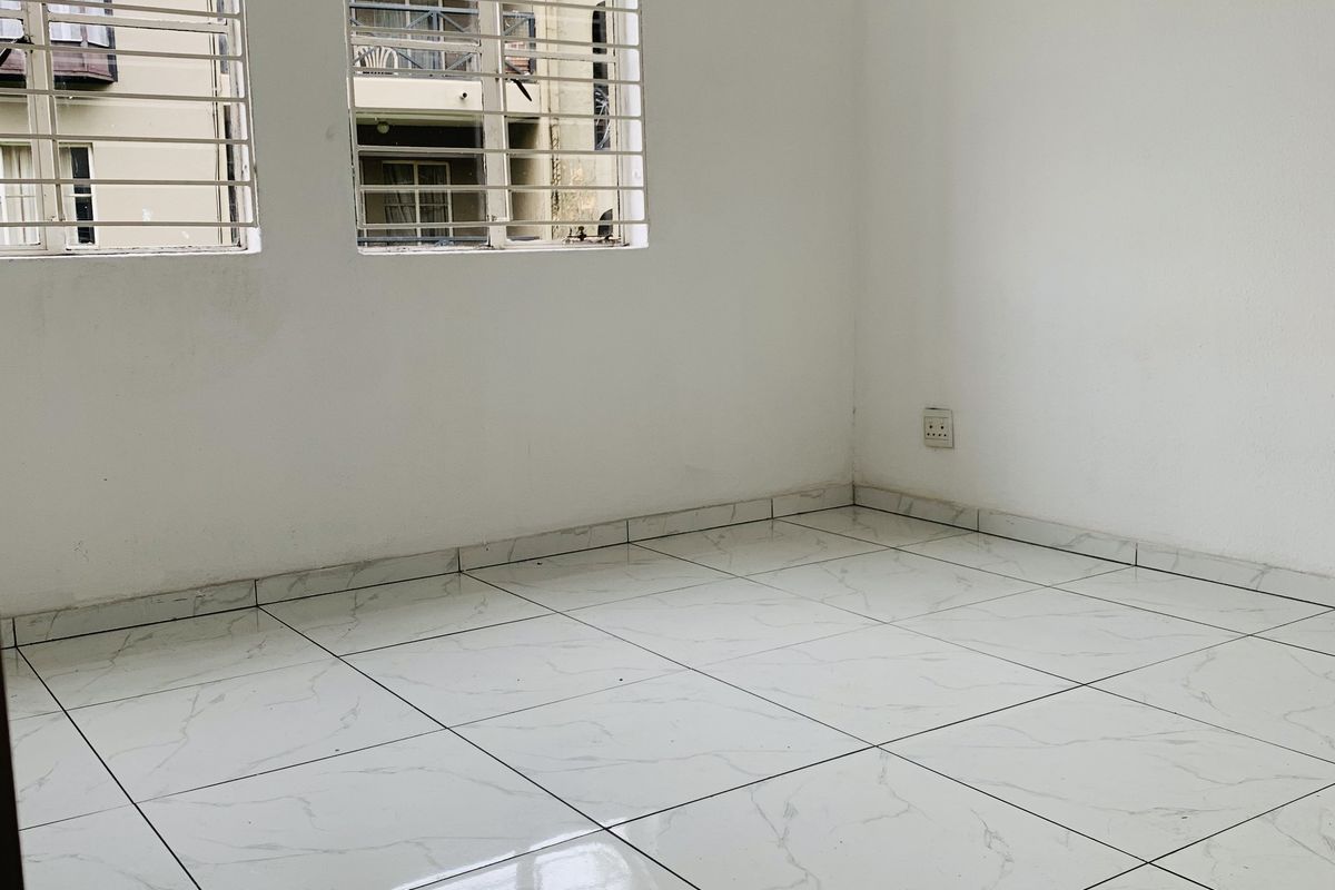 An empty bedroom featuring white marble-look tiled flooring and windows fitted with security bars.
