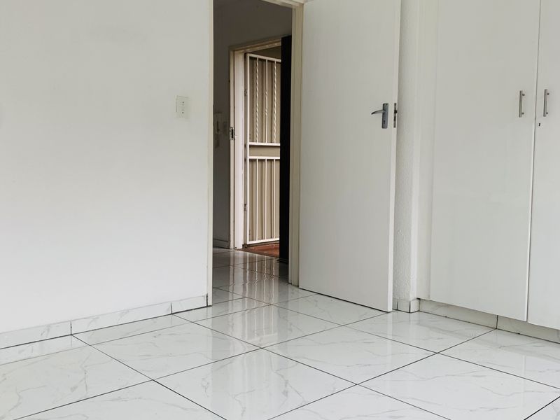 A bright, empty bedroom featuring modern white marble-look floor tiles and built-in cupboards, offering a clean and neutral space ready for personalization.