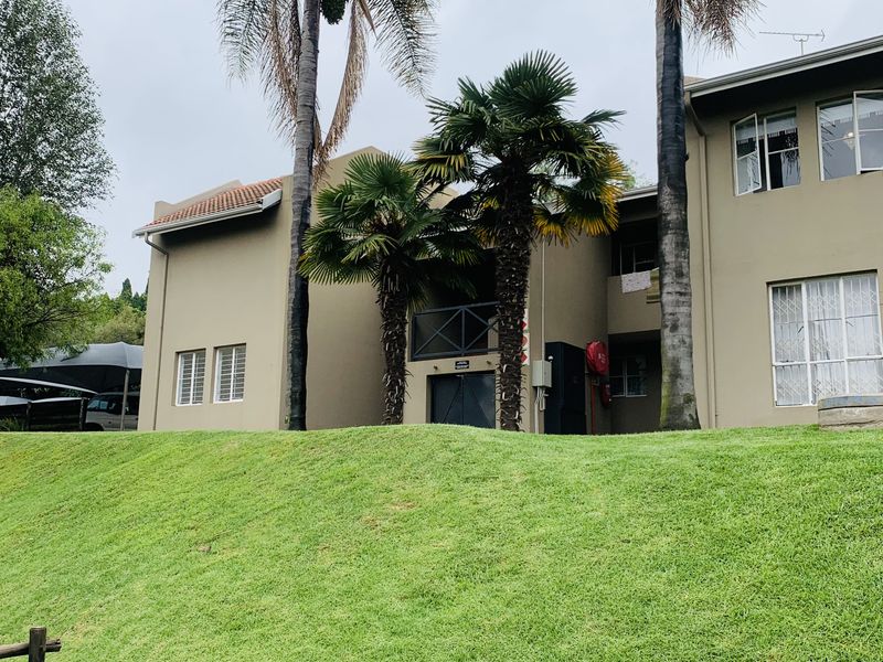 Rear view of the apartment building featuring a landscaped lawn, mature palm trees, and exterior building facade with security window bars.