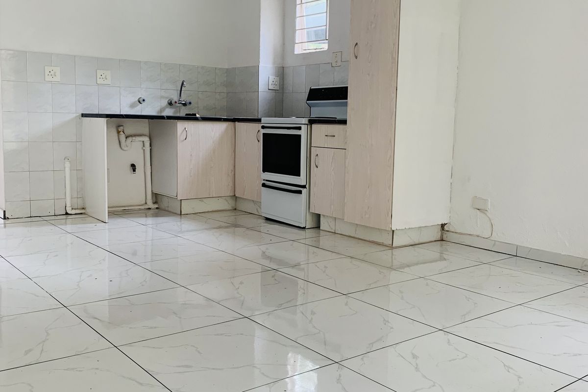 A functional kitchen area featuring white tiled flooring, built-in cabinetry, a tiled backsplash, and a freestanding oven, currently in need of minor repairs.