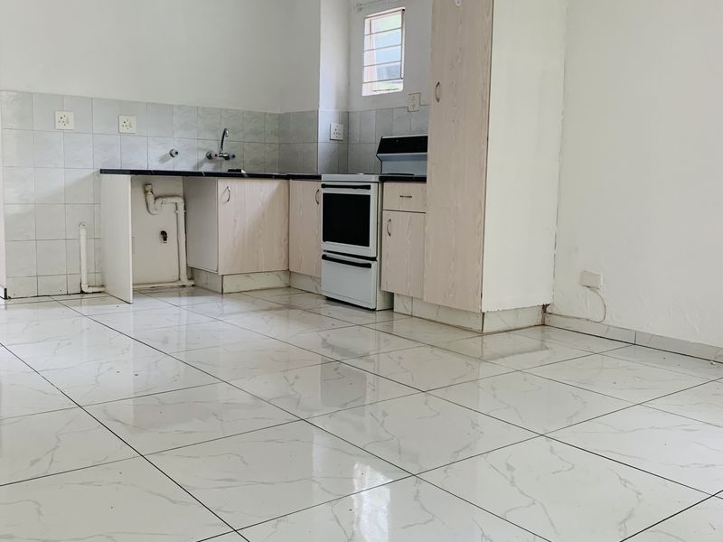 A functional kitchen area featuring white tiled flooring, built-in cabinetry, a tiled backsplash, and a freestanding oven, currently in need of minor repairs.