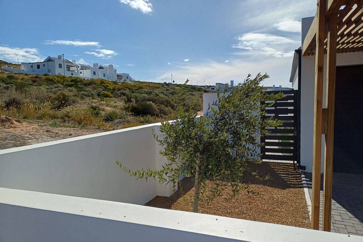 A view of the exterior side area featuring a low boundary wall, gravel landscaping, a timber pergola structure, and a gated entrance.