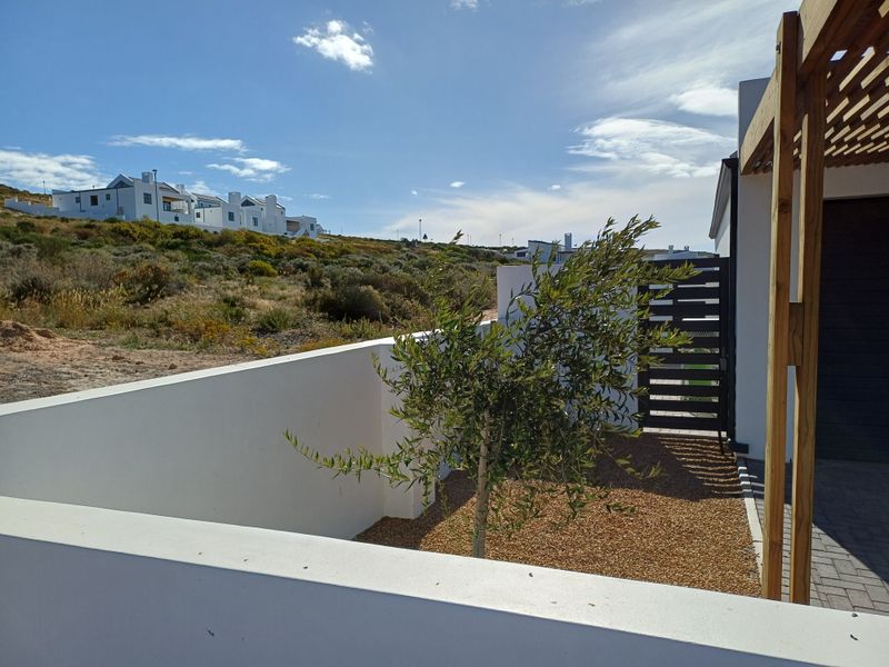 A view of the exterior side area featuring a low boundary wall, gravel landscaping, a timber pergola structure, and a gated entrance.