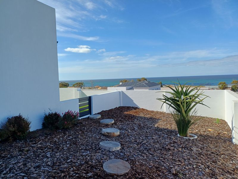 A modern rooftop terrace or balcony area featuring white perimeter walls, wood chip landscaping, and expansive ocean views.