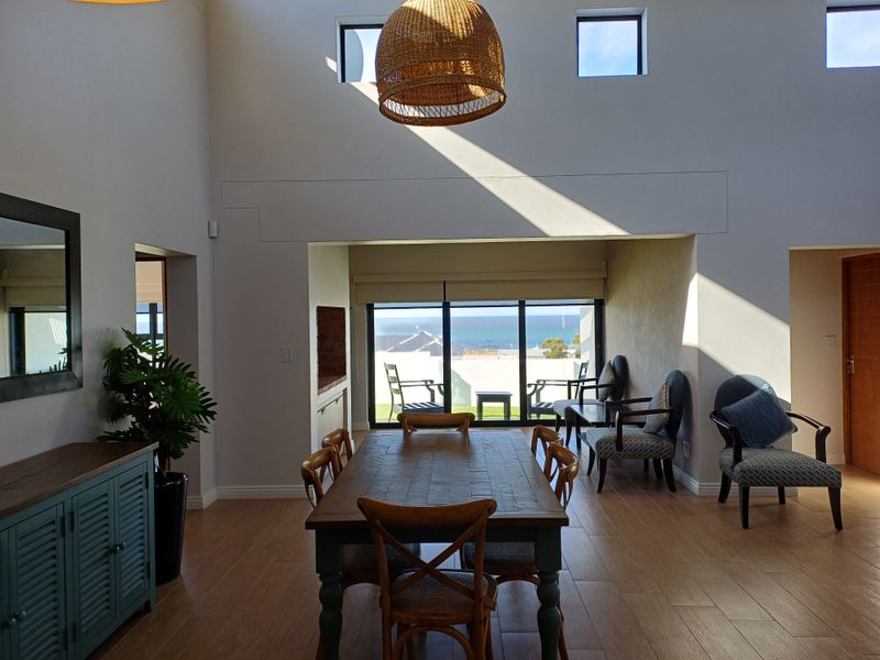 Spacious open-plan living and dining area featuring high ceilings, large windows, and sliding doors leading to a patio with ocean views.