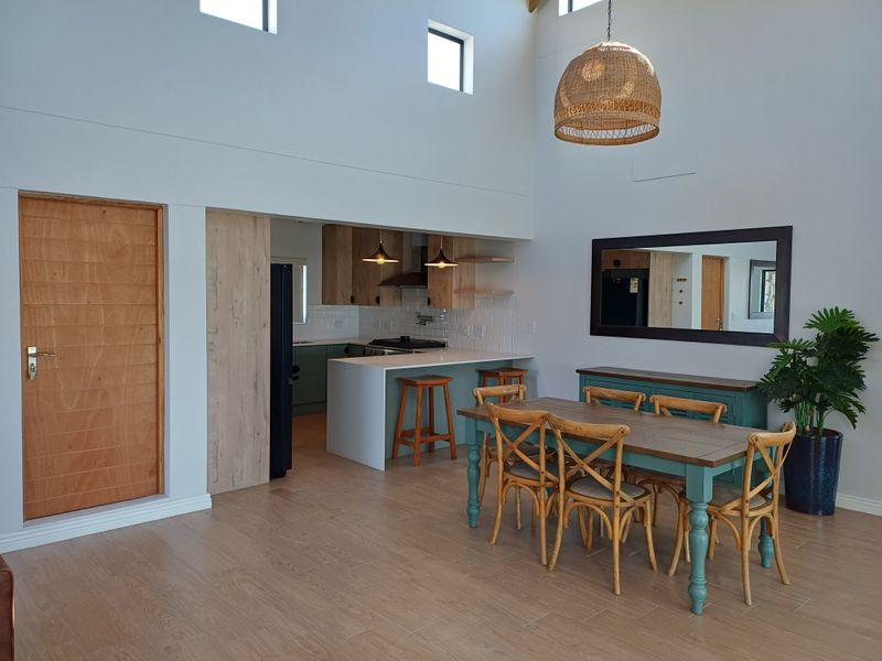 Open-plan living and dining area featuring a modern kitchen with breakfast bar, high ceilings, and wood-look tile flooring.