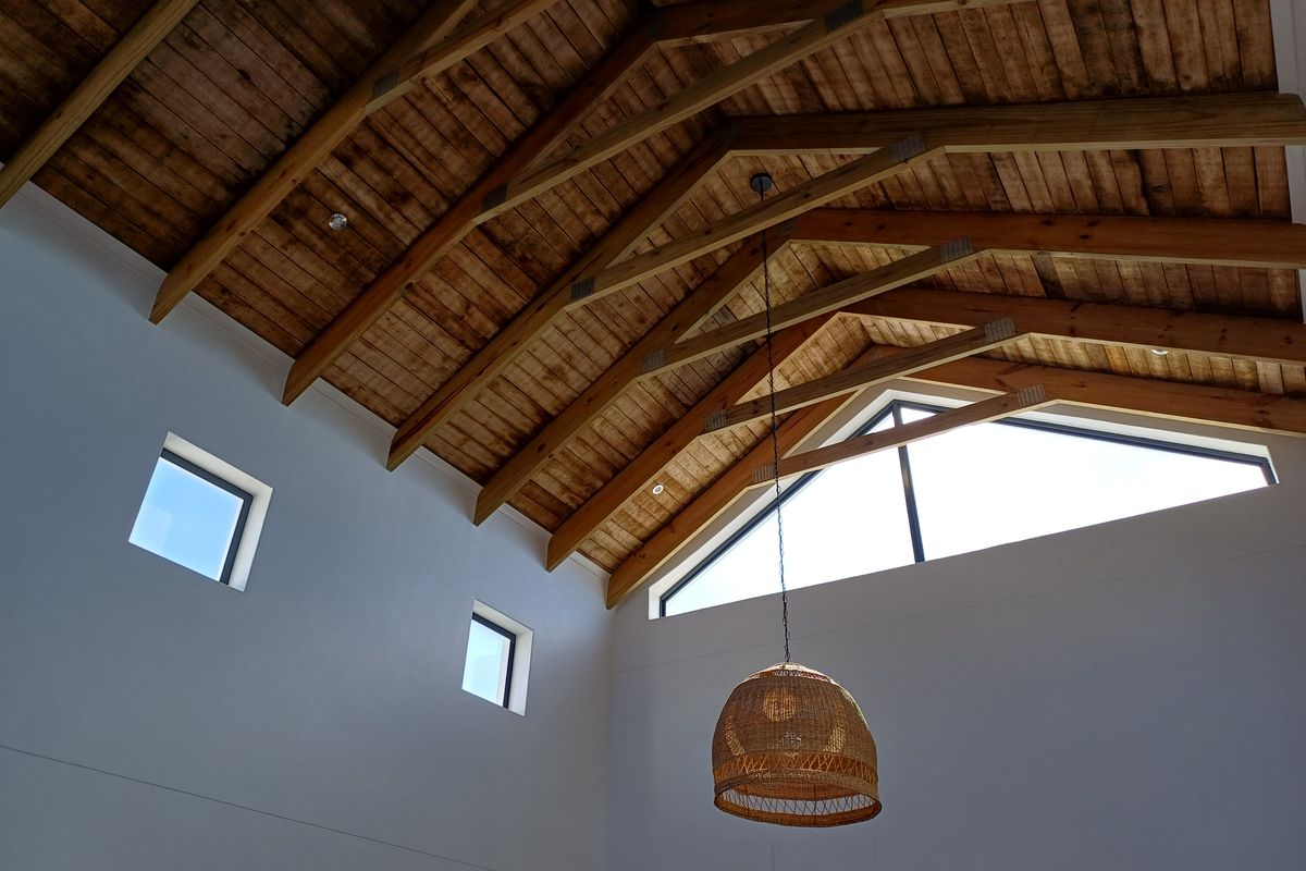 A bright living area featuring a high vaulted ceiling with exposed timber trusses and large triangular windows that provide ample natural light.