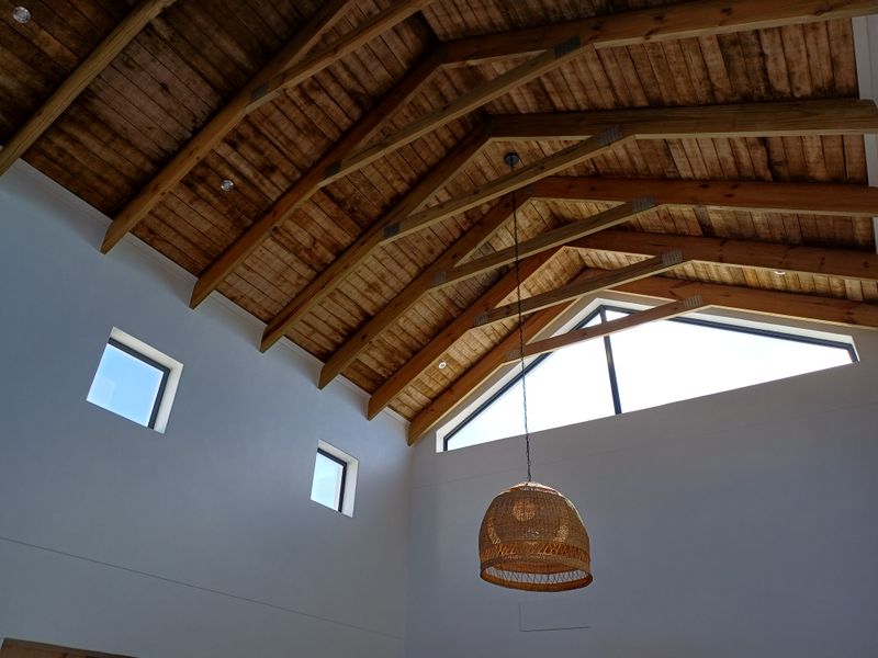 A bright living area featuring a high vaulted ceiling with exposed timber trusses and large triangular windows that provide ample natural light.