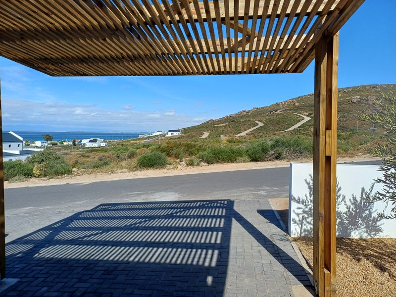 A covered outdoor patio area featuring a timber pergola structure, overlooking a coastal landscape with scenic hill and ocean views.