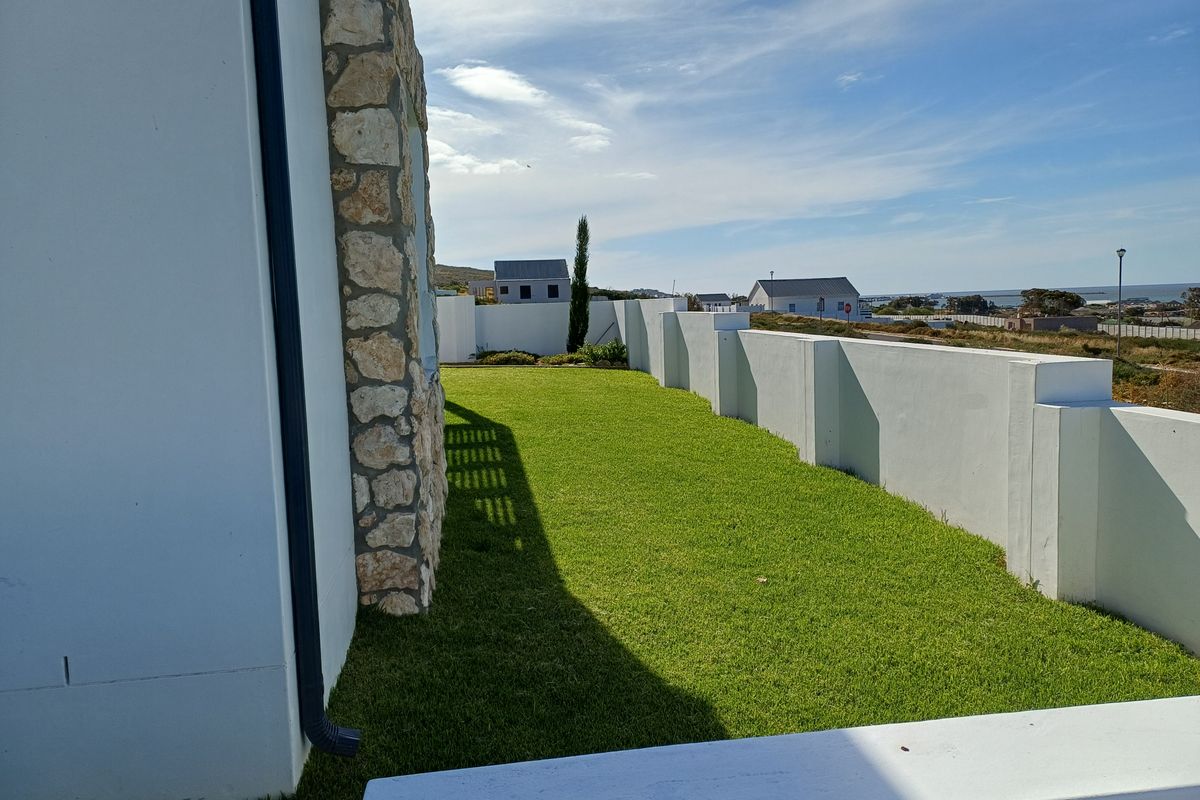 A well-maintained side garden featuring a manicured lawn, stone-clad wall detail, and perimeter boundary walls.