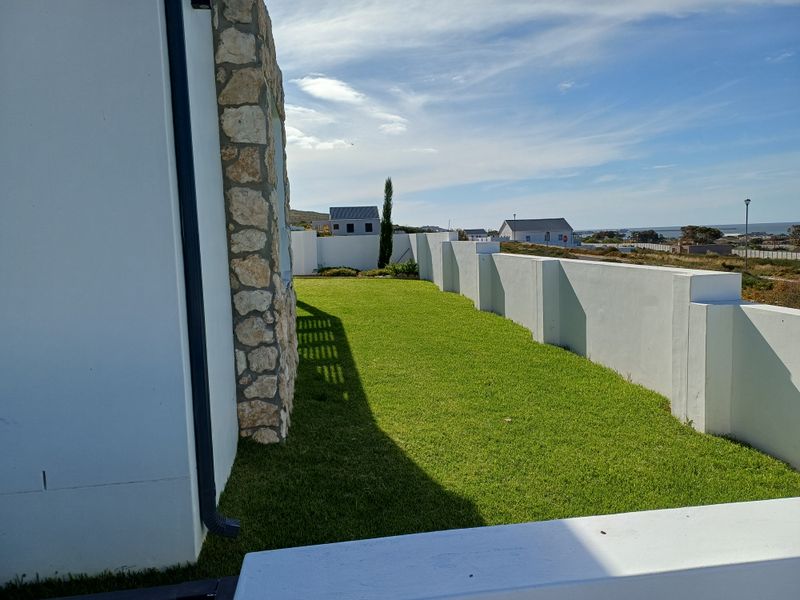 A well-maintained side garden featuring a manicured lawn, stone-clad wall detail, and perimeter boundary walls.