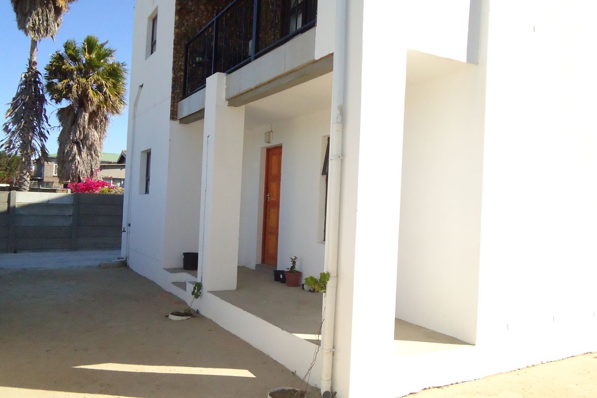 Rear exterior view of the property featuring a covered patio area, a balcony with metal railing, and concrete structural pillars.