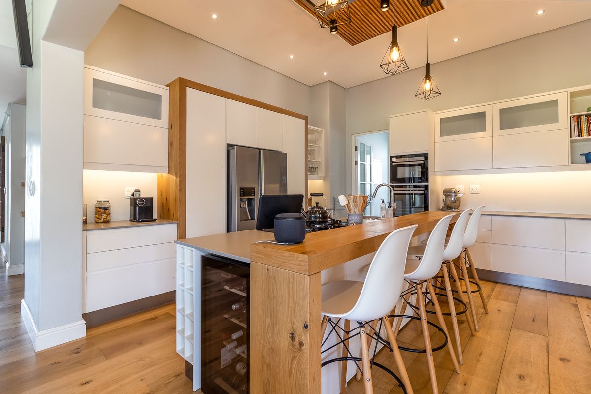 Modern kitchen featuring white cabinetry, integrated appliances, a wooden breakfast bar, and recessed ceiling lighting with a decorative timber feature.