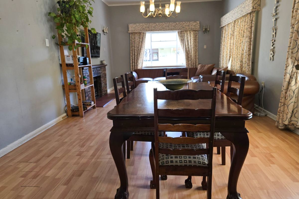 Spacious living and dining area featuring a stone fireplace, laminate flooring, and a central chandelier, offering a functional layout for family gatherings.