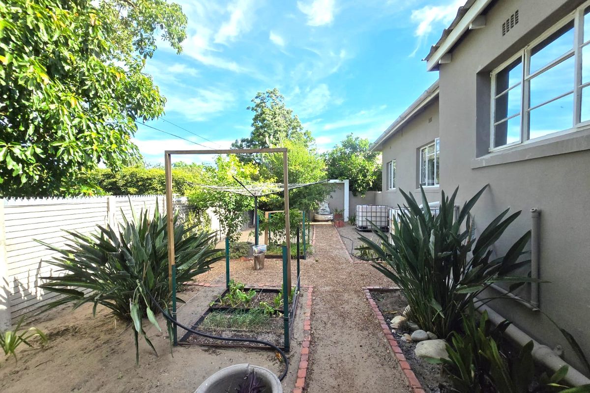 A well-maintained rear garden featuring a gravel pathway, brick-edged garden beds, and established perimeter fencing alongside the house exterior.