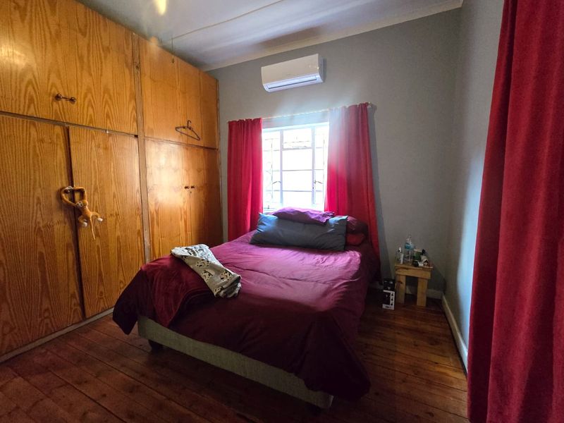 A bedroom featuring timber flooring, built-in wooden cupboards, and a wall-mounted split-system air conditioner.